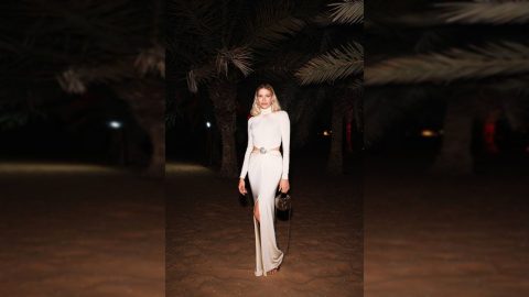 lena perminova poses gracefully on dubai's coastline, with the blue sea and modern skyline in the background, showcasing her effortless style.